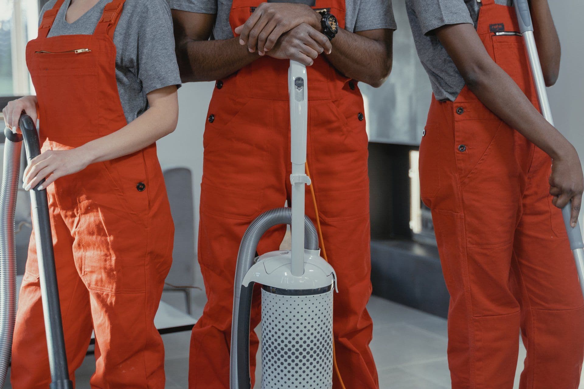 Three people in orange work suits standing next to each other holding a vacuum cleaner
